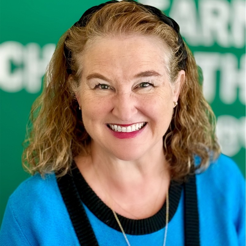 Middle aged white woman smiling for headshot, red lipstick and bright blue blouse with silver necklace