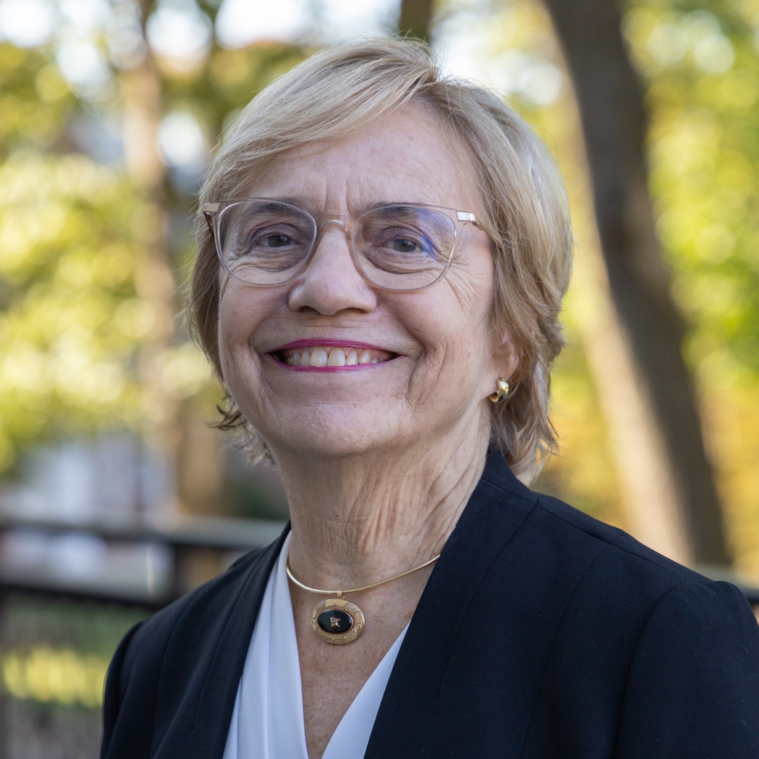 headshot of older white woman with blonde hair and blue eyes wearing glasses with a white shirt and dark blazer. She is smiling and looking at the camera.