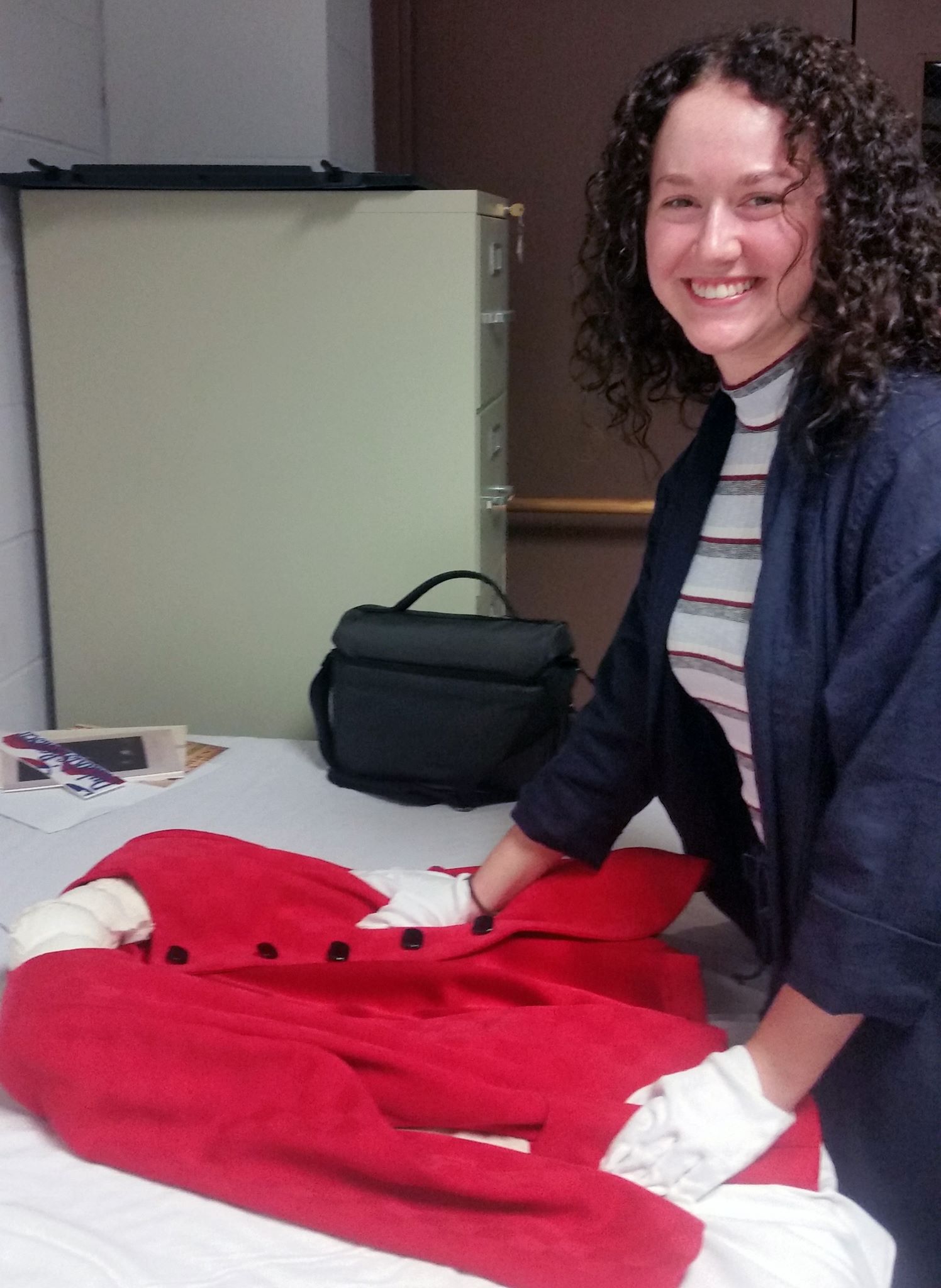 A woman stands over a white table with a red coat on top of it.